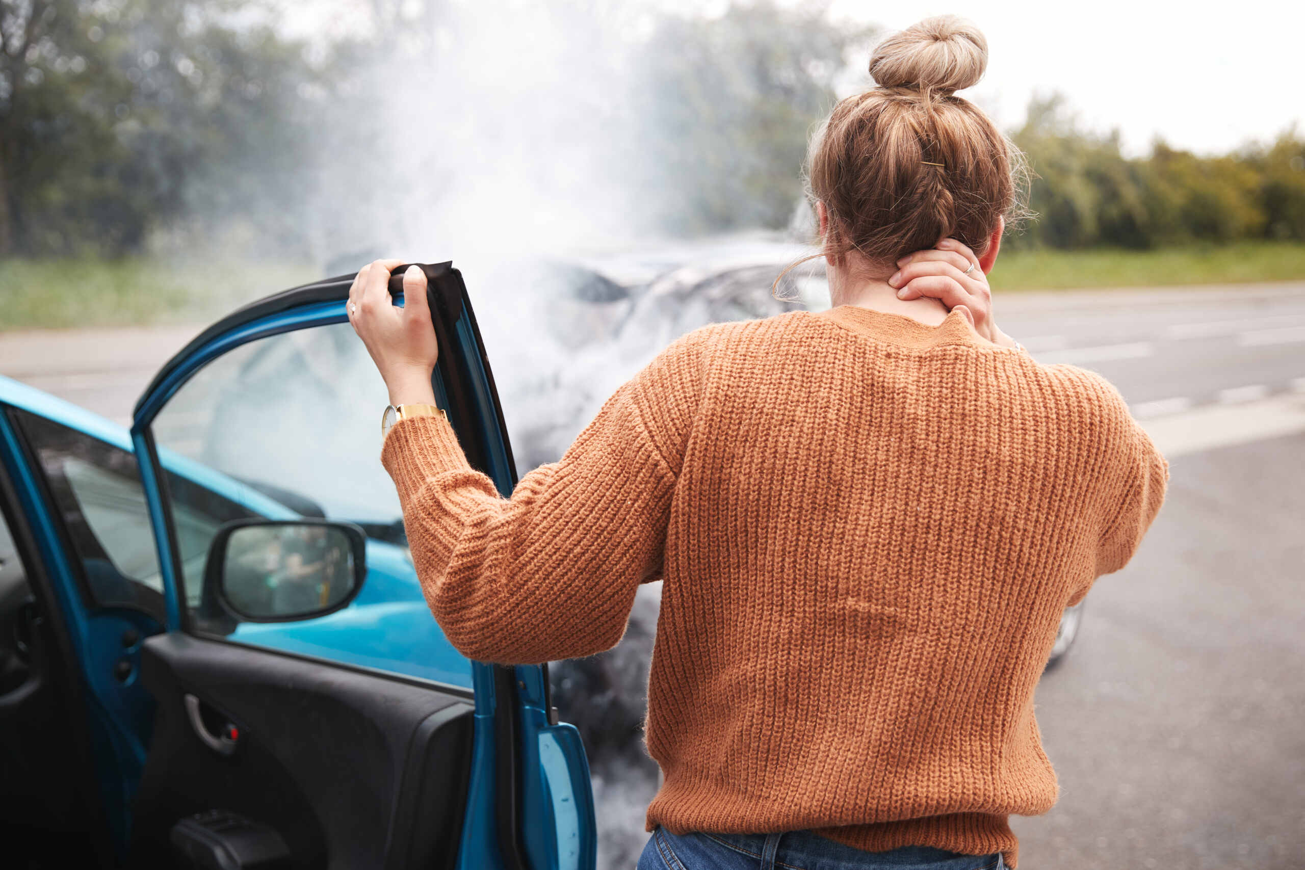 Woman holding the back of her neck after stepping out of a smoking crashed car.