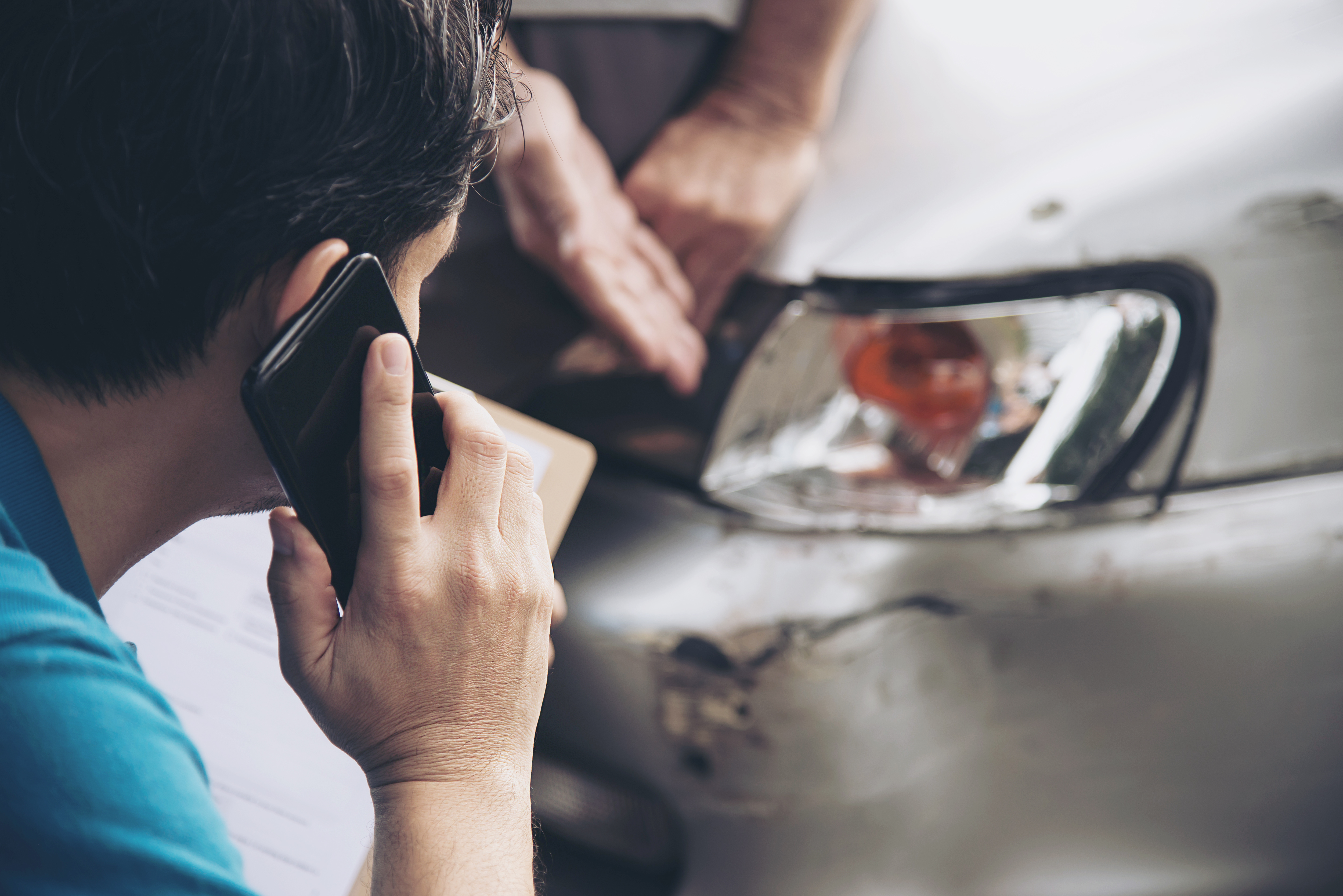 insurance agent on the phone in front of a car that has been damaged 