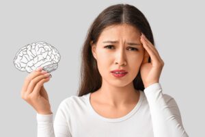 Woman touching her temple in pain while holding a paper cutout drawing of a human brain.