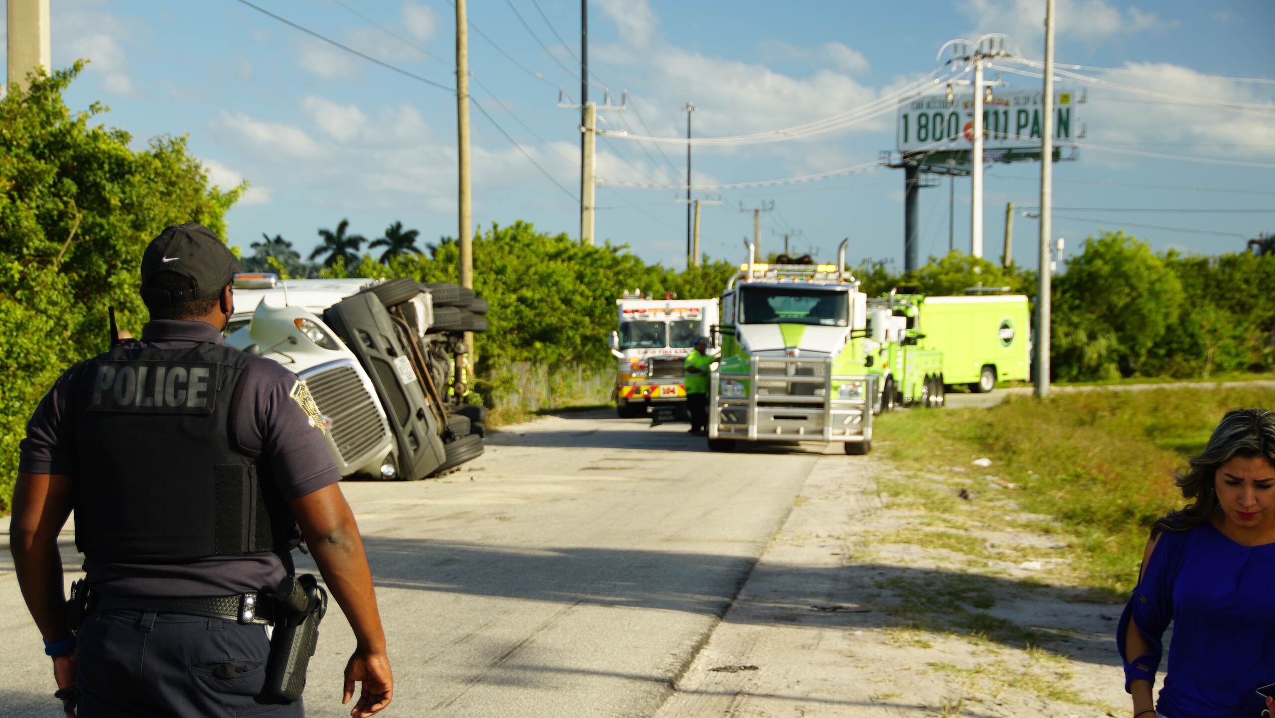 Police officer walking toward an overturned semi truck and emergency response vehicles.