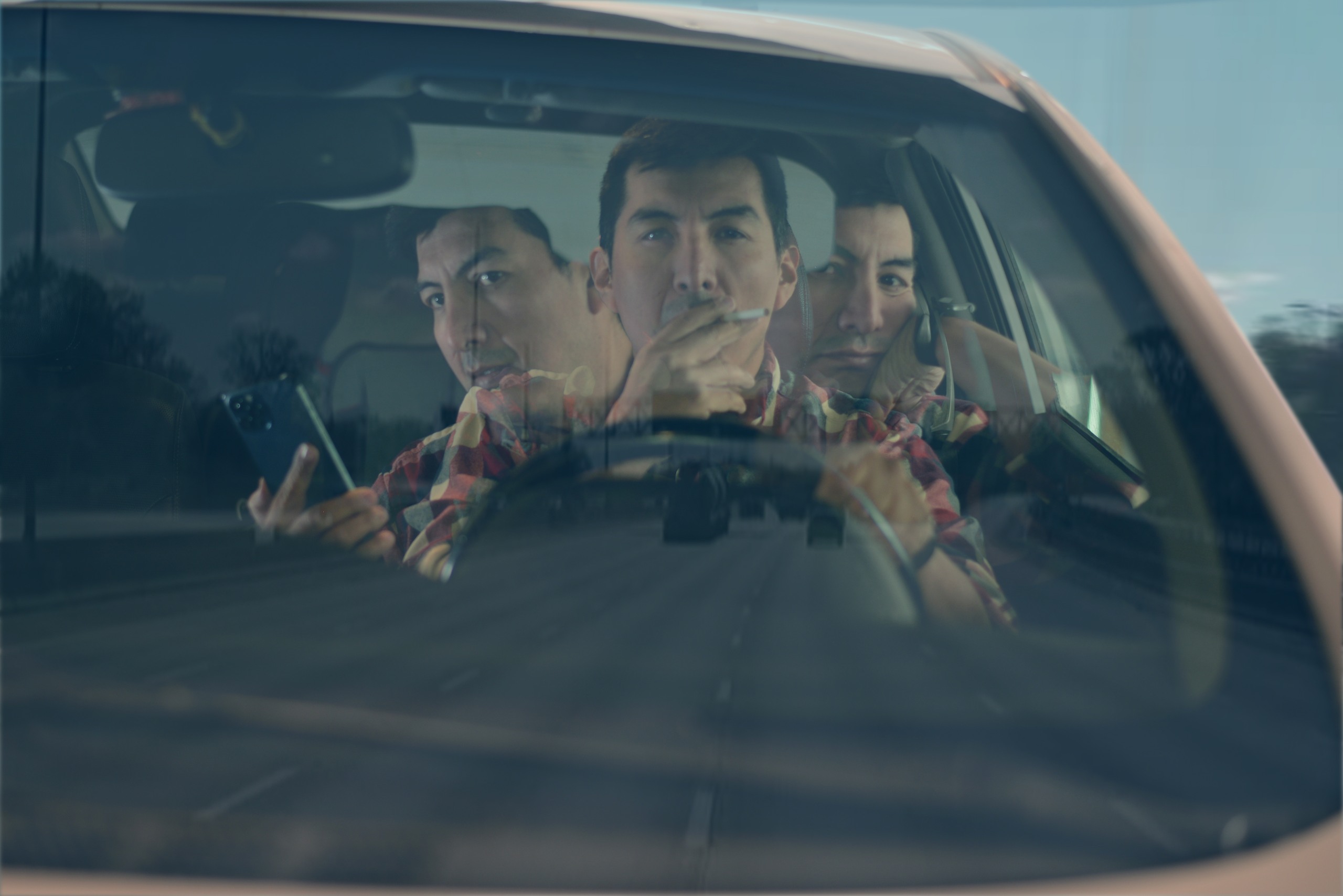Multiple exposure shot of a male driver smoking a cigarette and holding a smartphone behind the windshield.