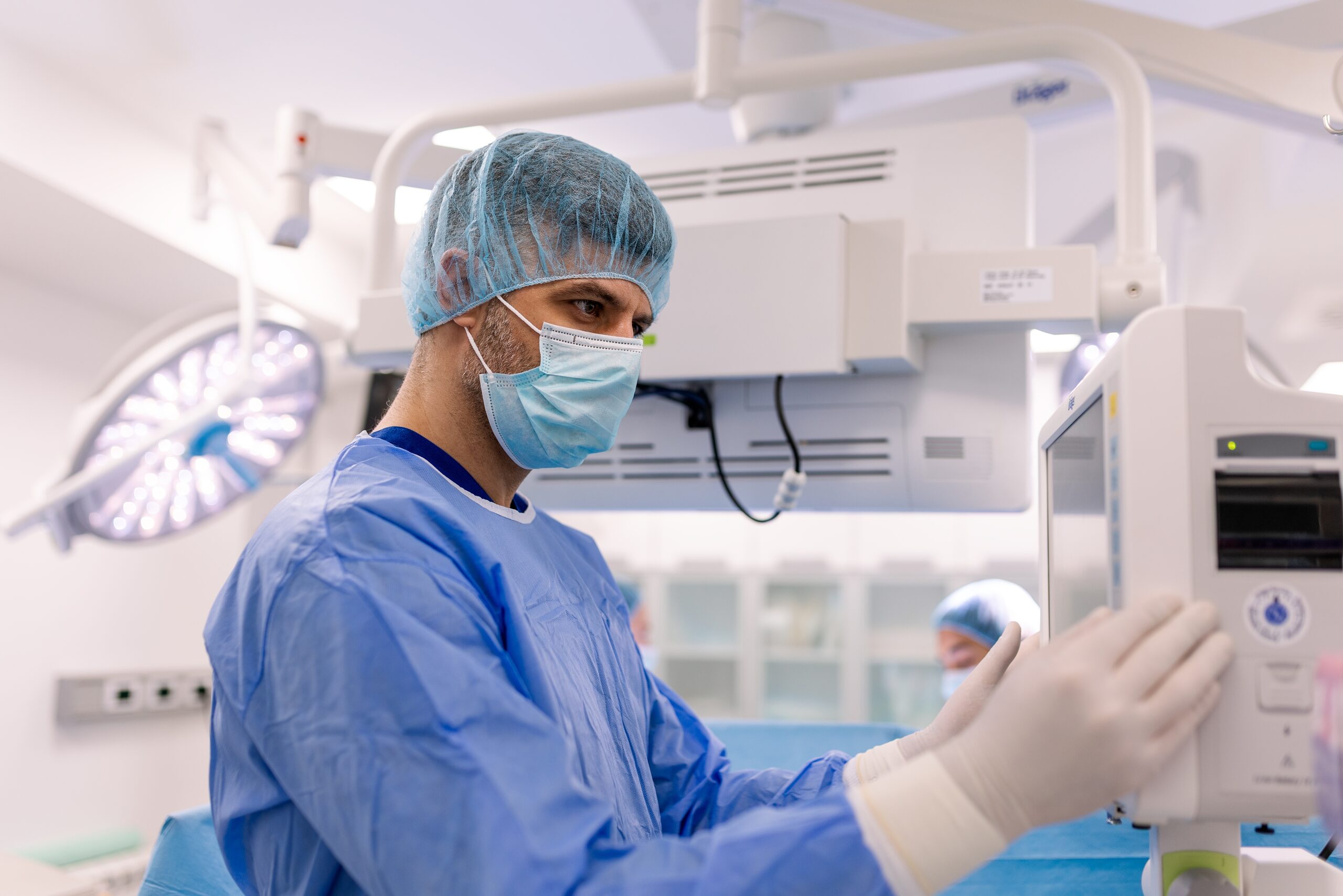 Surgeon in scrubs and a mask adjusting medical equipment in an operating room.